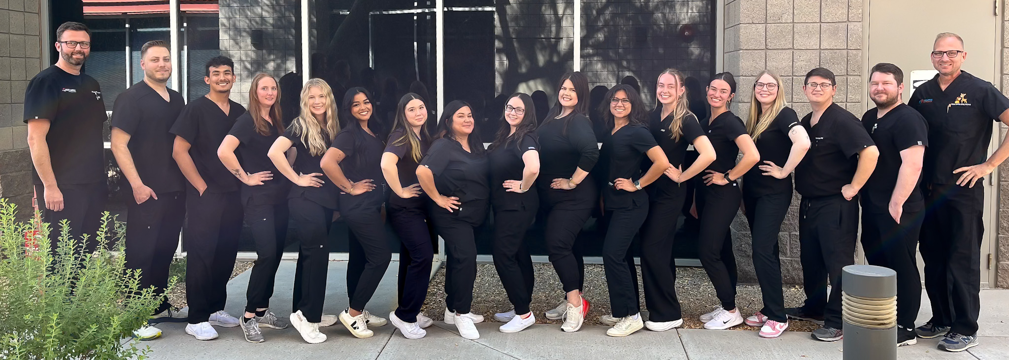 people lined up wearing black scrubs smiling a the camera