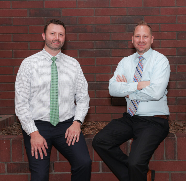 image of two male doctors sitting who are doctors with a red brick background